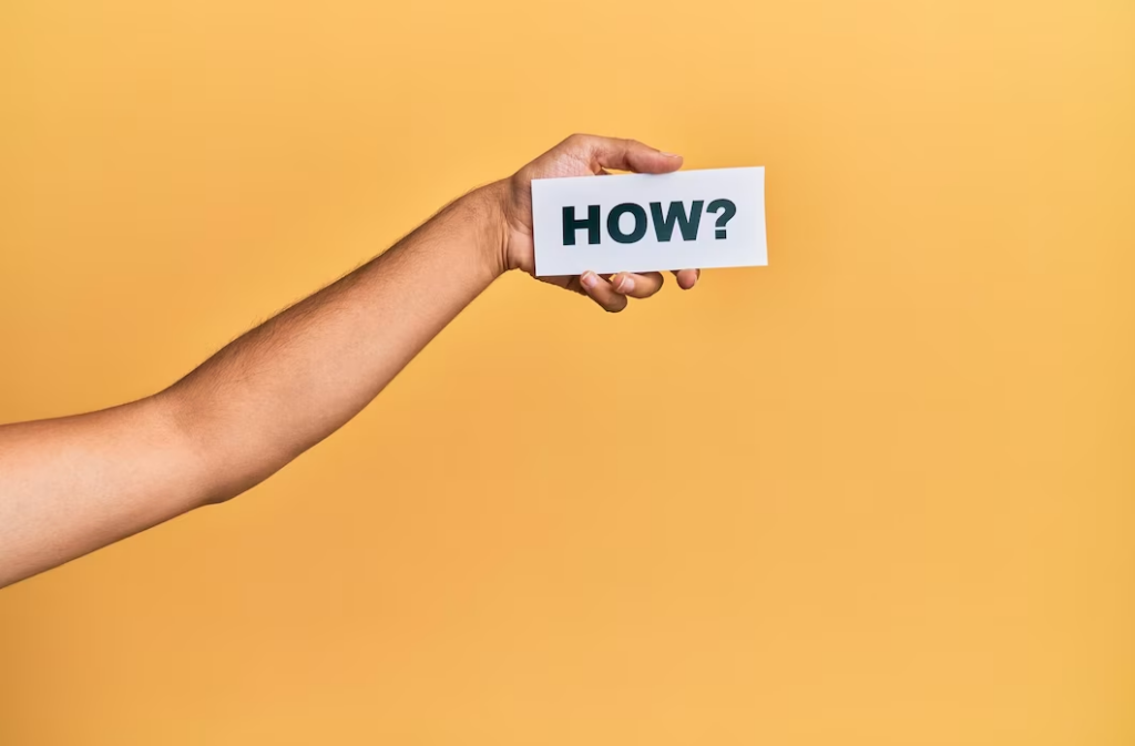 Hand holding a paper with the word 'how' against a yellow background